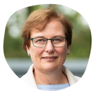 Auf dem Bild ist eine Frau mit Brille und kurzen Haaren zu sehen, die freundlich in die Kamera schaut.